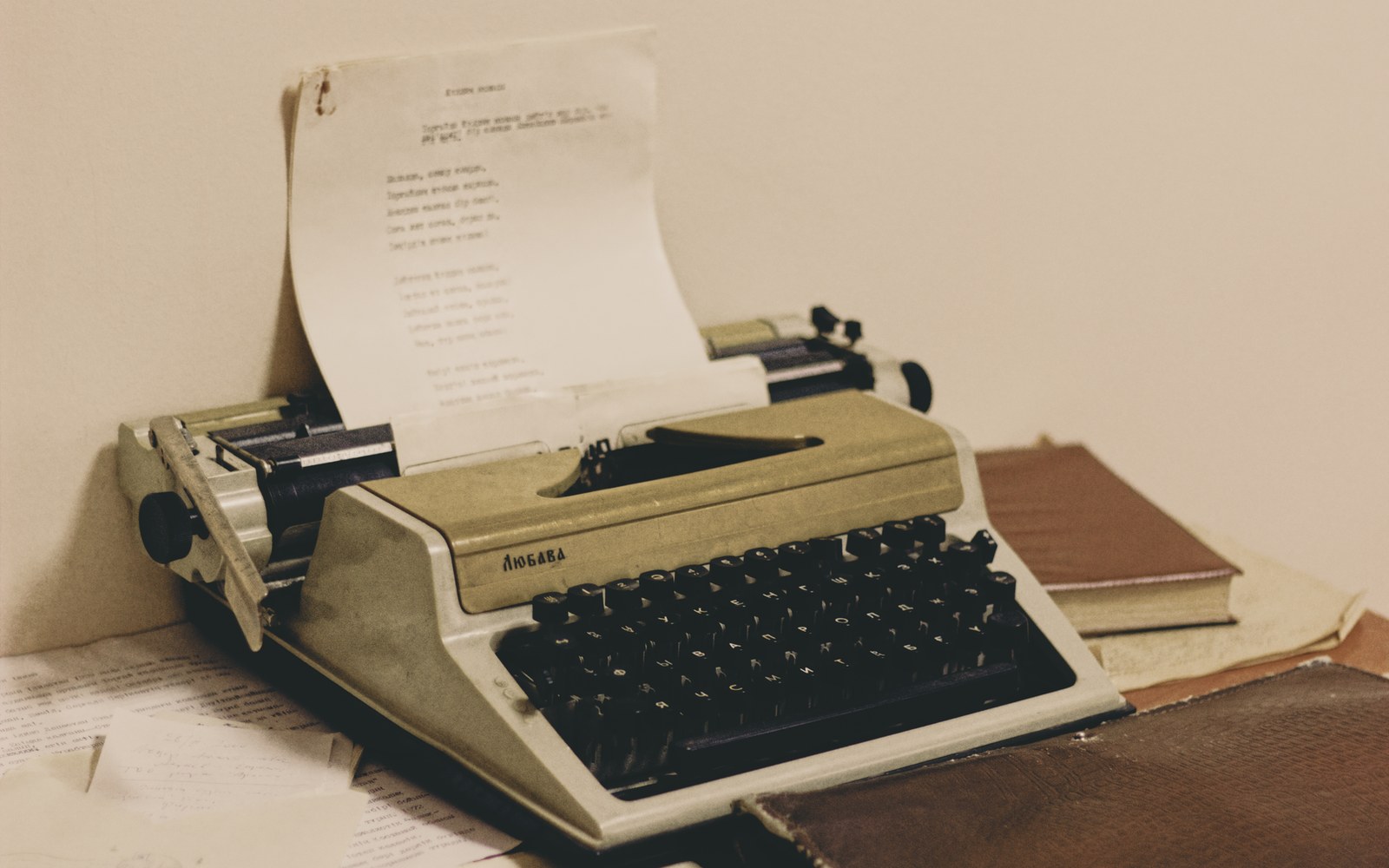 A vintage typewriter with a typed page loaded, beside a leather-bound book and papers