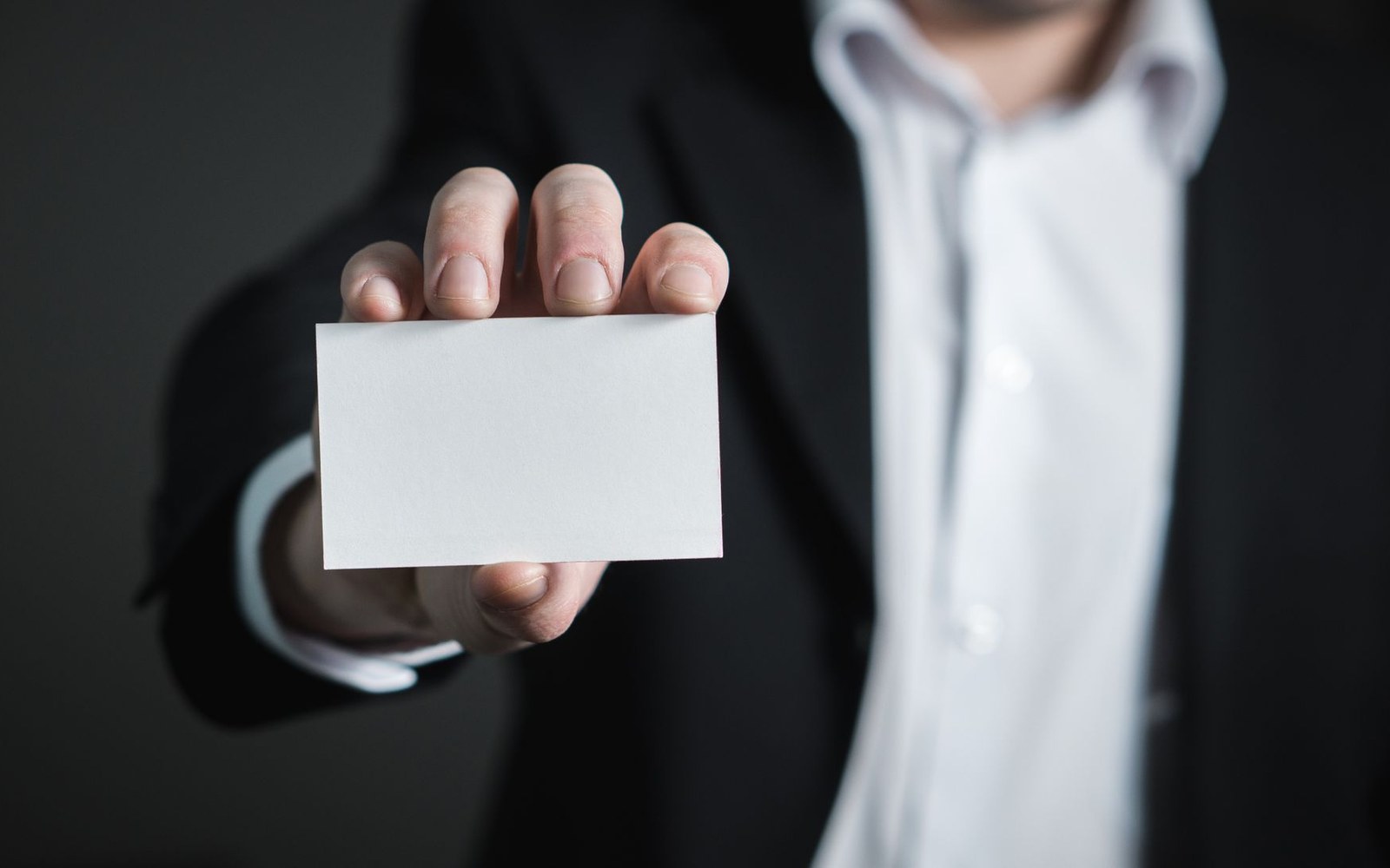 Man in a suit jacket holding out a blank white business card