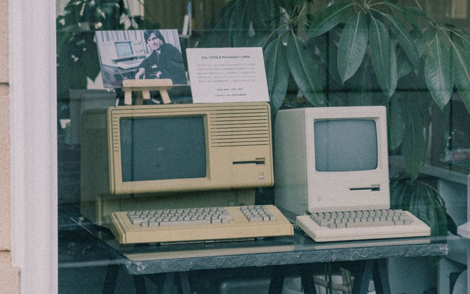 Vintage Apple Lisa and Macintosh computers displayed in a shop window with an information card