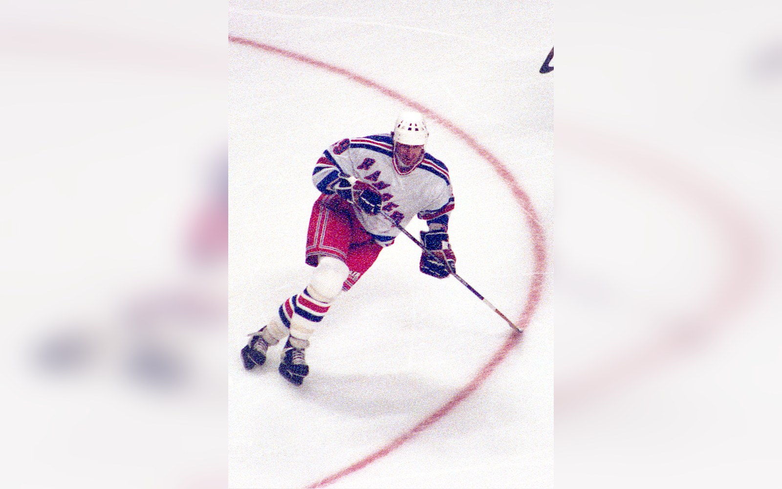 Rangers hockey player skating with stick near the faceoff circle on ice