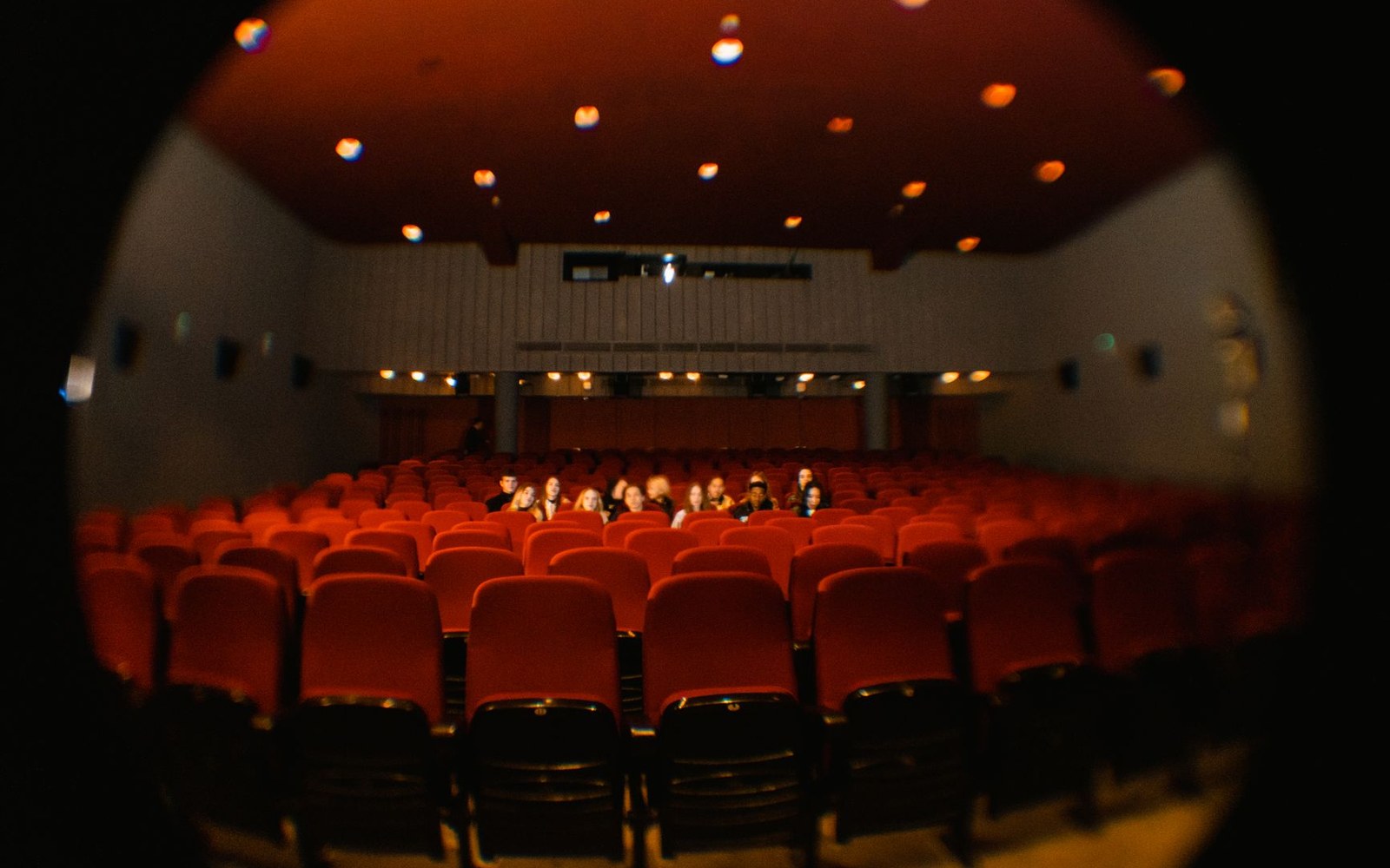 Adult audience in a keynote hall, faces lit from the projection screen, wide landscape